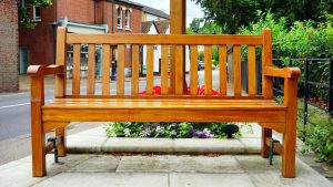 A wooden bench is placed in an urban street surrounded by vibrant flowers.