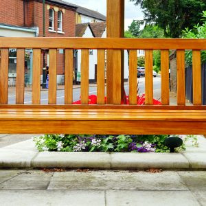 A wooden bench is placed in an urban street surrounded by vibrant flowers.